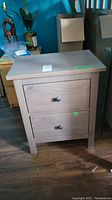 Front view of pine bedside table showing two drawers with round knobs and wood grain finish.