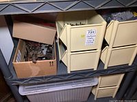 Two shelves filled with various plastic stackable bins and a cardboard box filled with assorted hand tools, mainly metal wrenches, pliers, and cutting tools.