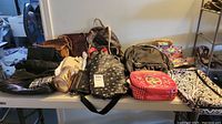 Full overview of all purses, wallets, and lunchbox spread out on table showing variety of colors and styles.