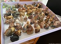 Wide shot of the collection showing numerous animal and human figurines packed in a tray with white paper.