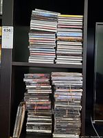 Four stacks of CD jewel cases on a black shelving unit, two on the top shelf and two on the bottom shelf