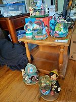 Group shot of multiple Disney snow globes on a wooden side table and floor.
