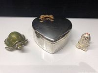 Front view of the three items in the lot showing the heart-shaped box, turtle, and dog figurine on a black surface.