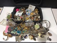 Overview of entire lot showing assorted costume jewelry pieces piled in a black container, including bracelets, earrings, pendants and trinkets.