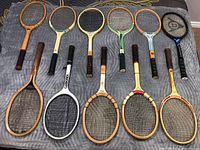Full overhead view of all 11 tennis rackets laid out flat showing various colors and handle grips.
