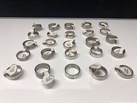 Photo showing the assortment of 25 stainless steel rings arranged in rows, with size labels attached for identification.