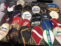 Full layout of 30 tennis racket protectors of various brands, colors, and styles.