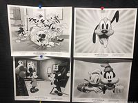 Four black and white Disney prints pinned on a black background. Characters include Mickey Mouse, Minnie Mouse, Goofy, Donald Duck, and Pluto in birthday-themed scenes.