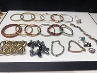 Wide shot showing complete assortment of bangles, bracelets, rings, and earrings laid out evenly on a white surface.