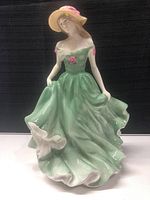 Front view of the porcelain figurine showing the green dress, pink rose details, and beige hat.