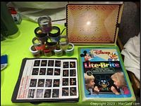 Overview of vintage Lite-Brite peg board illuminated with multiple containers of colored pegs, black stencil sheets, and refill book