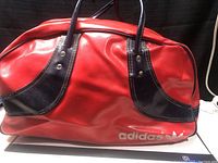 Side view of red vintage Adidas sports bag with black accents and white Adidas logo and trefoil