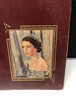Cover of the scrapbook with a color portrait of The Queen wearing a tiara and pearl necklace on a dark red textured background with gold-colored border accents.