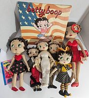 Full view of the seven Betty Boop plush dolls arranged in front of a Betty Boop 2005 calendar with an American flag background.