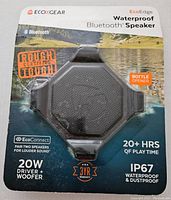 Front view of EcoXGear EcoEdge waterproof Bluetooth speaker in original packaging showing branding, 'Rough Certified Tough' badge, 20W driver + woofer, 20+ hours playtime, IP67 waterproof and dustproof rating, and bottle opener feature.
