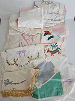 Lot of folded embroidered vintage linens in white, cream, and pastel colors with multiple lace and embroidery patterns visible.
