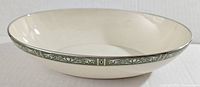 Side view of oval Lenox Adrienne bowl showing cream color and decorative green and white vine patterned rim with black accent line.