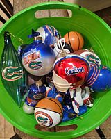 Green bin filled with various Florida Gators Christmas ornaments including balls, sports helmets, and character figures.