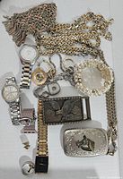 Overview of assorted jewelry, watches, chains, and belt buckles displayed together on white background.
