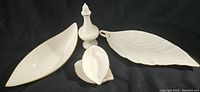 Four vintage Lenox porcelain items on black background: three leaf-shaped trays of different sizes and one finial-shaped decorative piece with white and gold details.