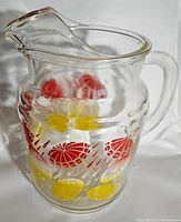 Side view of clear glass pitcher showing colorful red and yellow umbrella and raindrop design.
