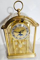 Full view of the vintage Bulova anniversary clock showing gold-tone frame, glass dome, clock face with Roman numerals, and crystal pendulum.