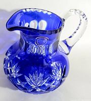 Front angle view showing cobalt blue body, clear handle, and cut-glass starburst pattern on pitcher.