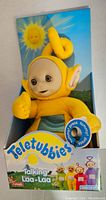Full front view of Laa Laa doll in original packaging showing the yellow plush doll with curled head antenna and the Teletubbies logo on the front of the box.