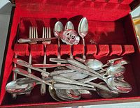 Overview of silverware in red velvet-lined box showing forks, spoons, and servers scattered in slots