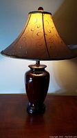 Lamp lit showing brown urn base and taupe textured fabric shade with swirl pattern.