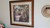 Full view of the framed art print hanging on a wall, showing the tropical garden scene and the frame design.