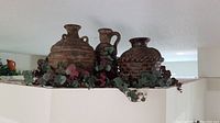 Photo of three clay decorative pots with artificial greenery beneath, showing rustic finishes and various shapes.