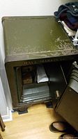 View of closed top and front side of green metal floor safe with worn paint and 'HALL MARVIN CO.' lettering visible.