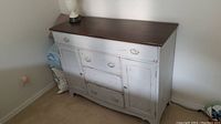 Front view of side board showing distressed caulk painted finish with some scuffs, multiple drawers and cabinets. Top surface is dark wood. Some fabric on side visible.