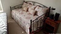 Front view of black metal daybed with paisley coverlet and accent pillows