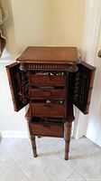Front view of closed jewelry chest showing four drawers and two side compartments doors open, no contents.