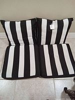 Four black and white vertically striped chair cushions arranged in two pairs, two seat cushions and two back cushions, visible padding and fabric texture.