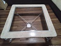 Top-down image showing square manufactured marble top with clear glass center and iron framing.