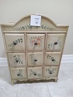 Front view of mini storage cabinet with nine drawers featuring floral painted designs and round knobs.