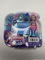 Front packaging of the Barbie Mermaid Power Chelsea doll and accessories, showing the doll with a mermaid tail and various small accessories, including a treasure chest.