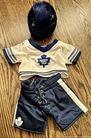Photo of the full Build-A-Bear Toronto Maple Leafs outfit including jersey, shorts, and helmet laid out on wooden floor.