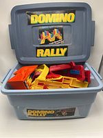 Gray plastic Domino Rally storage container with label shown, open with colorful plastic track pieces inside.