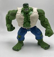 Front view of the green Incredible Hulk figure standing with muscular arms and ripped white shirt and blue pants.