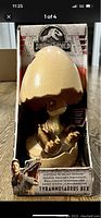 Front view of the Jurassic World Hatch N Play T-Rex figure in an egg shaped container inside original packaging showcasing dinosaur and branding details.