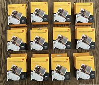Twelve Kodak Instant Print 3x3 film cartridge boxes arranged in a 4x3 grid on wooden floor