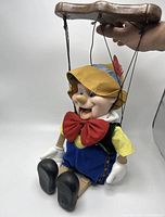 Full view of the Pinocchio marionette sitting, showing wooden control bar and attached strings