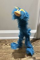 Front view of blue fluffy marionette puppet standing on a wooden floor.