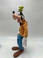 Side profile of vintage pose-able Disney Goofy figure showing fabric jacket, blue pants and yellow hat.