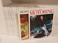 Photo showing multiple Architectural Digest magazines arranged vertically with two issues in front, including one titled Architectural Digest Motoring featuring a man leaning on a vintage green car.