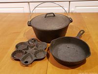 Overall view of the cast iron pots, skillet, and mold on a wooden table showing their size, shape and wear.